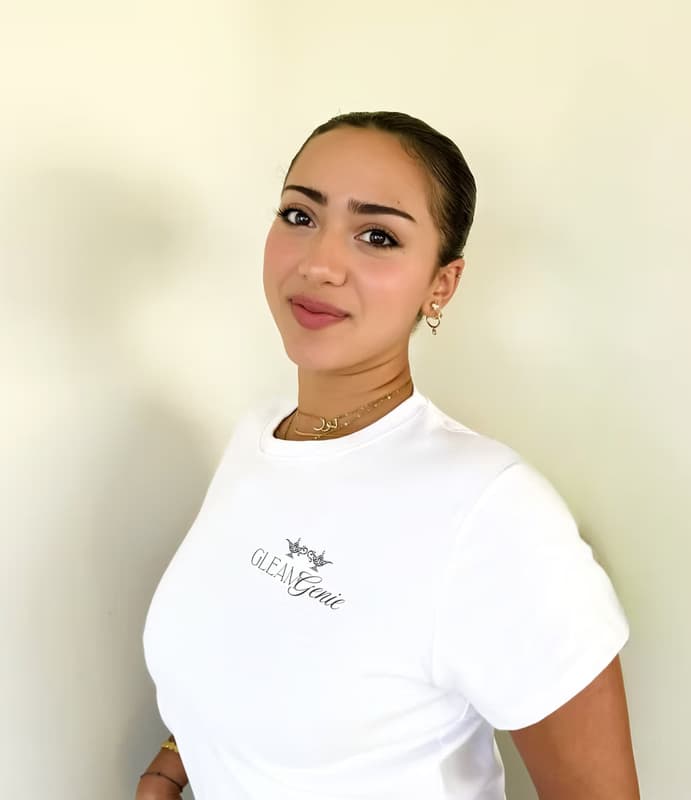 Norah, the founder of Gleam Genie, smiling in a white t-shirt with the company logo.